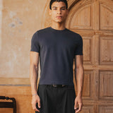 Man wearing a black t-shirt and pants standing in front of a wooden door.