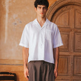 Man wearing a white shirt and brown pants standing in front of a wooden door.
