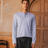 Man wearing a light blue long-sleeve shirt and dark pants standing in front of a wooden door.
