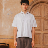 Man wearing a light-colored shirt and brown pants standing in front of a wooden door.