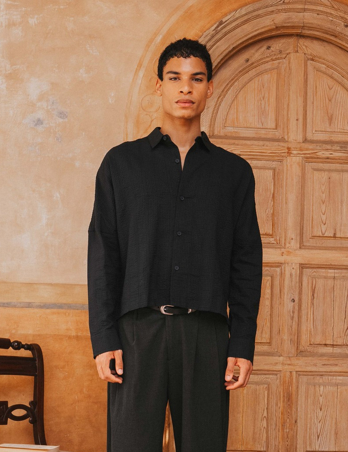 Man wearing a black shirt and pants standing in front of a wooden door.