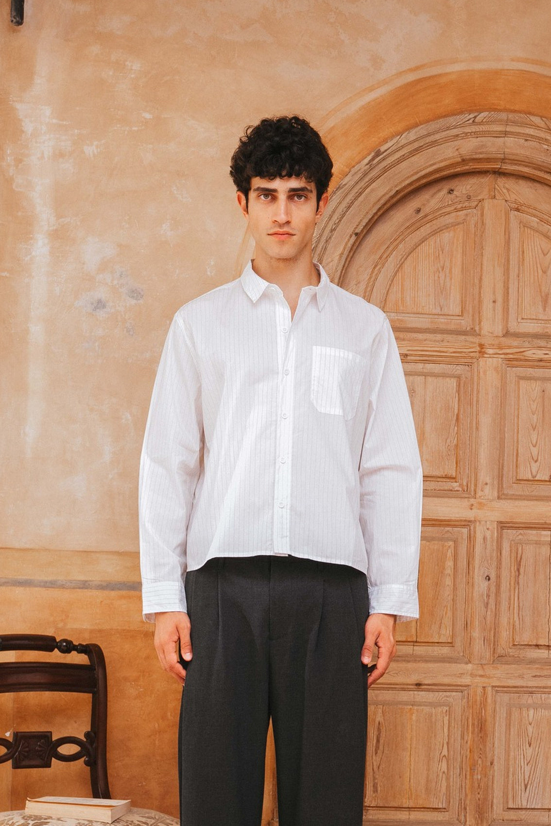 Man wearing a white shirt and black pants standing in front of a wooden door.