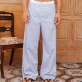 Man wearing light blue striped pants standing on a patterned floor with wooden paneling.