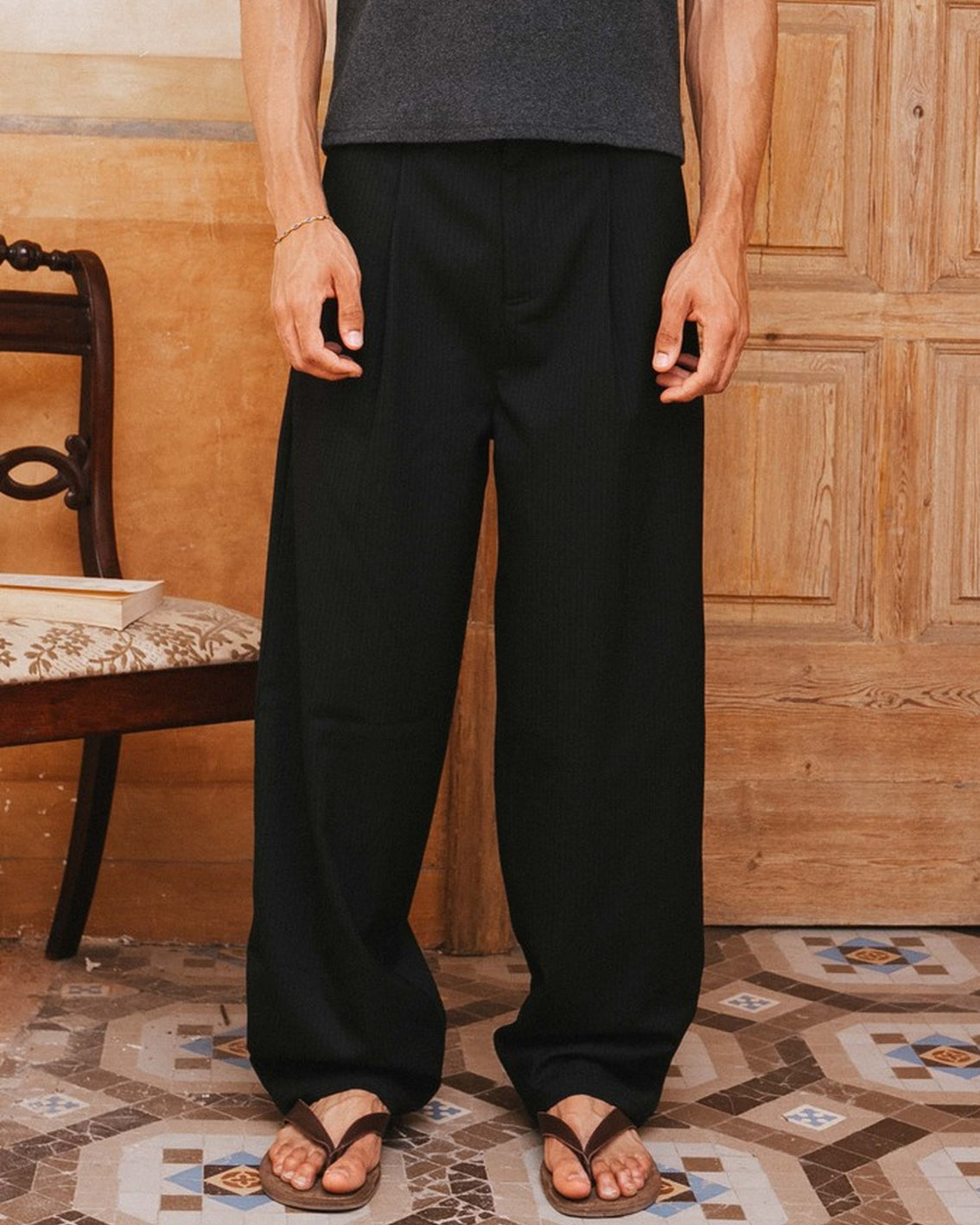 Person wearing black pants and a gray tank top standing in a room with wooden paneling and patterned floor.